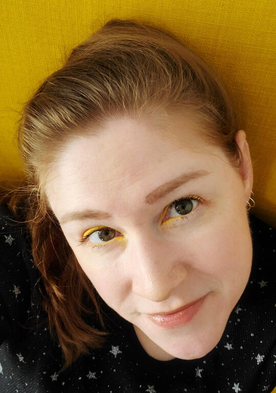 Author Photo A photo of a woman's face. She is looking directly at the camera, pale with reddish hair pulled back behind her head.